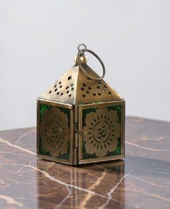 Farolillo de metal con flor y símbolo Om calado de 10 cm con luz de vela proyectando sombras espirituales.