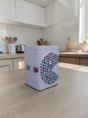 Lata comecocos para té 100g con diseño ilustrado de tazas y cierre metálico para conservación.